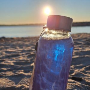 Une bouteille contenant de la phycocyanine est posée sur la plage avec un couché de soleil à Antibes