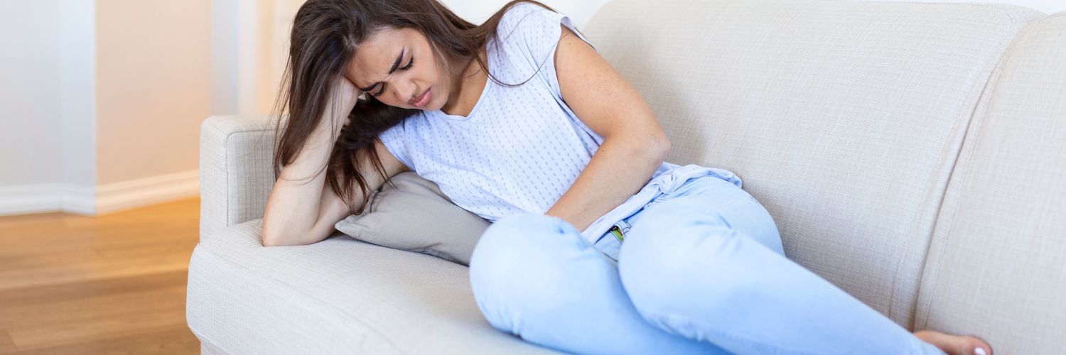 une femme est allongée sur son canapé et souffre de douleurs au ventre